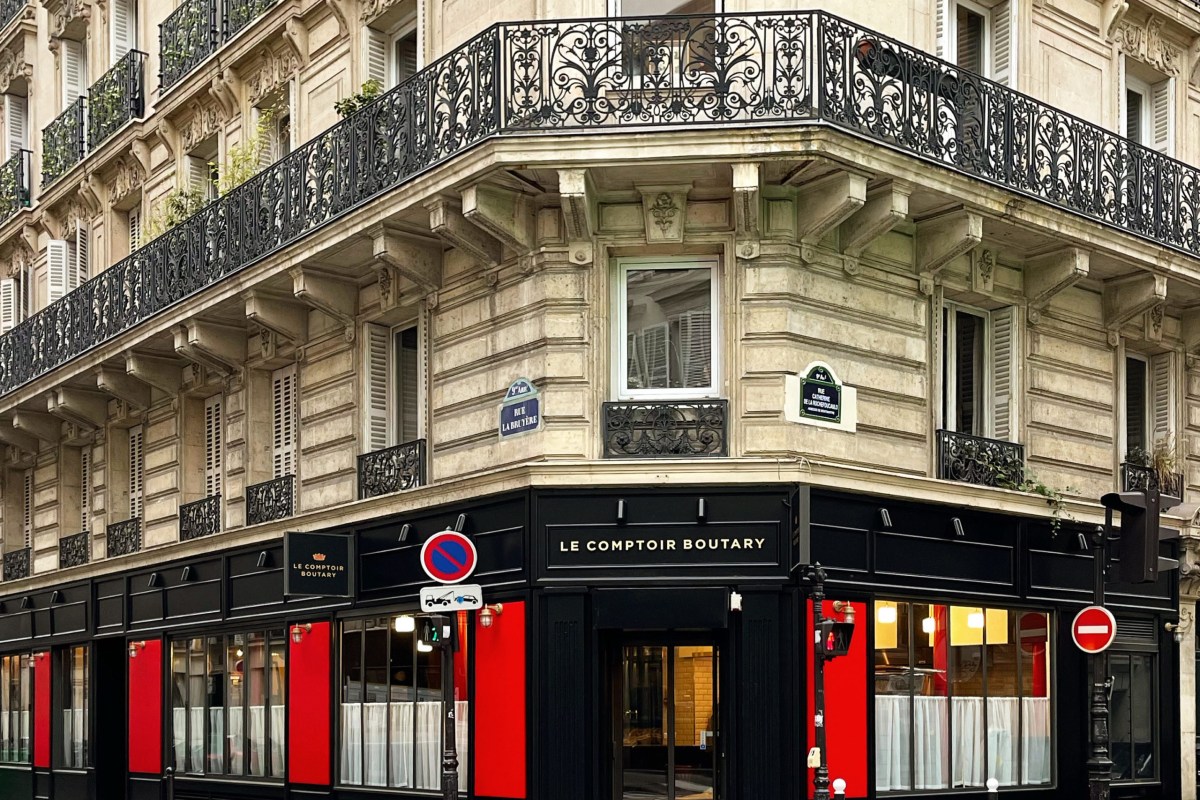 Corner view of Le Comptoir Boutary's black-and-red Parisian facade with signage, under ornate balconies