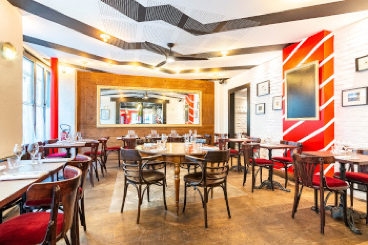 Restaurant dining room interior with wooden tables, red accents, and framed pictures on white brick walls