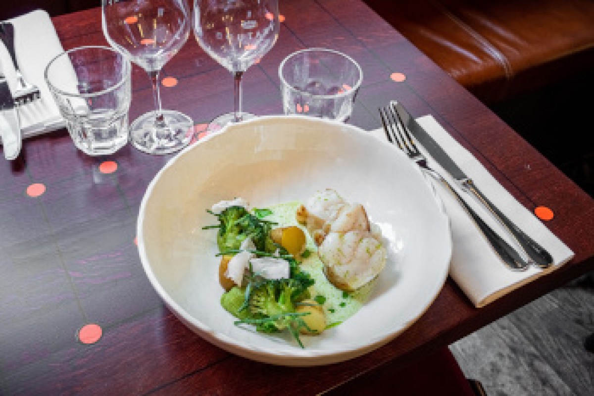 Plated seafood dish with potatoes and greens on a laid table with wine glasses and cutlery