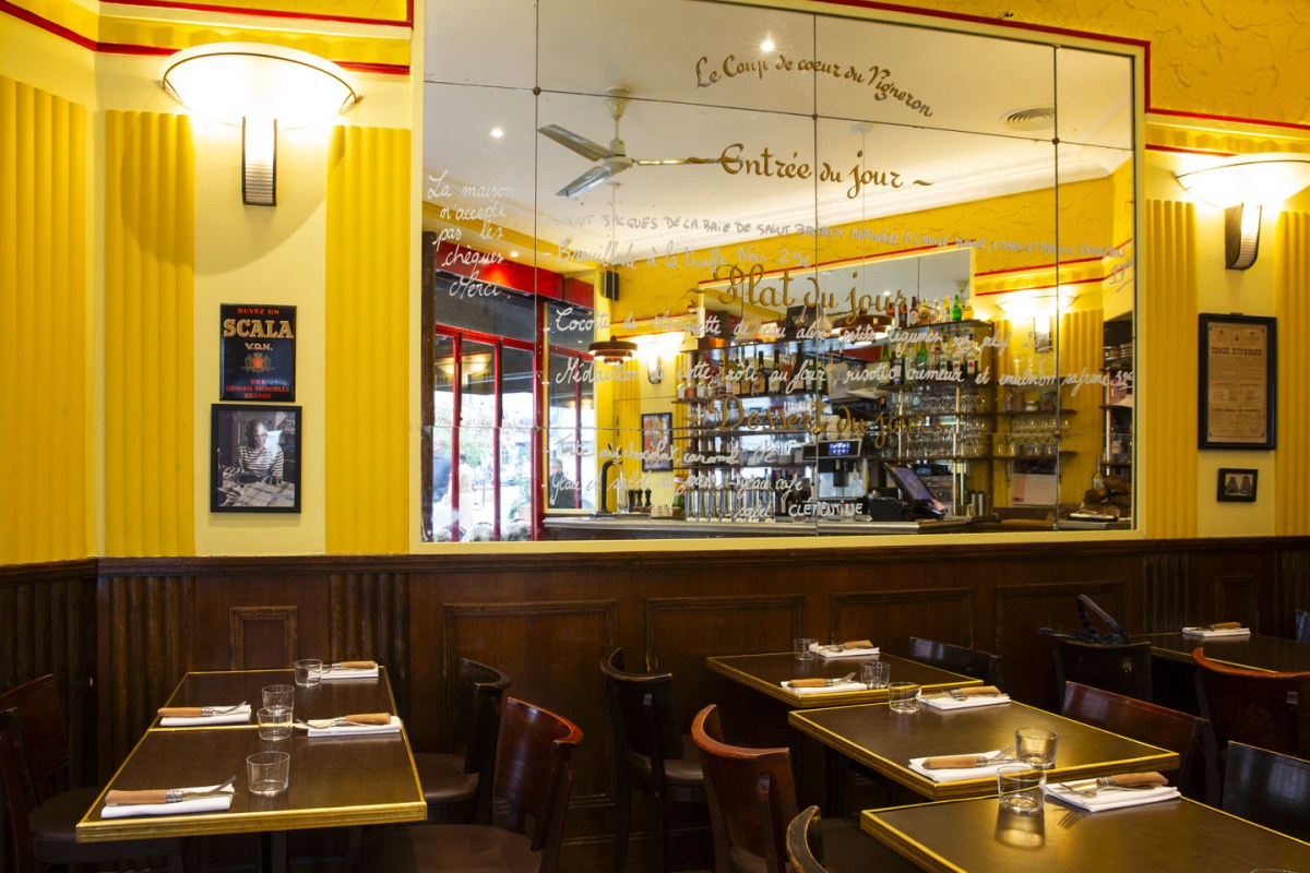 Interior dining room of Le Comptoir du Relais with yellow walls, a mirrored bar area, and set tables with wooden chairs.
