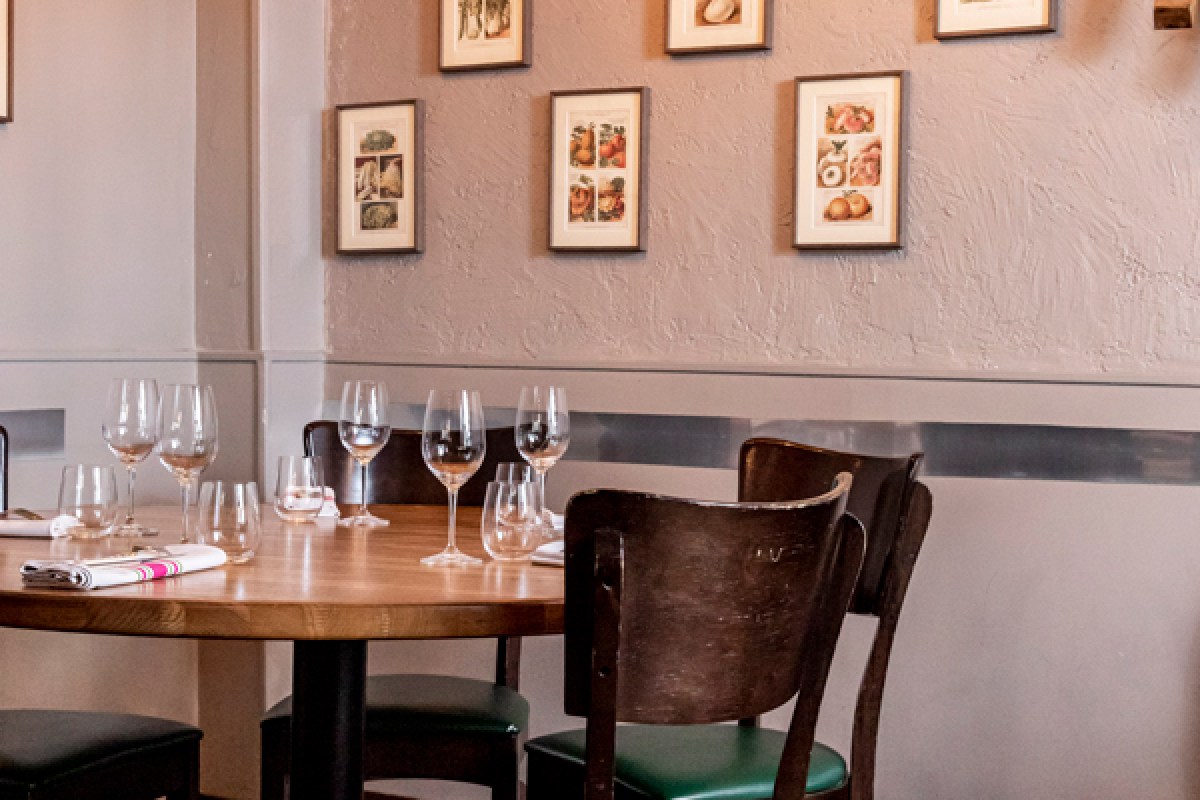 Dining room detail with set table, wine glasses, wooden chair, framed prints on wall