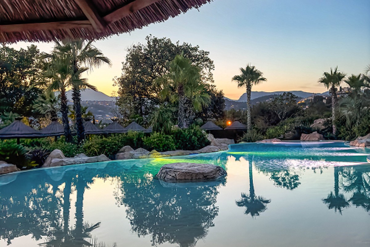 Infinity pool at sunset with palm trees and mountain silhouette