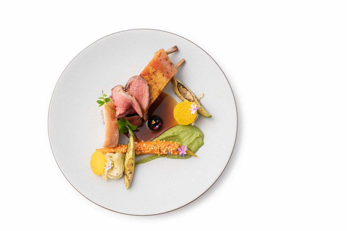 Artfully plated rack of lamb with vegetables, purée and flowers on a white plate, top-down view