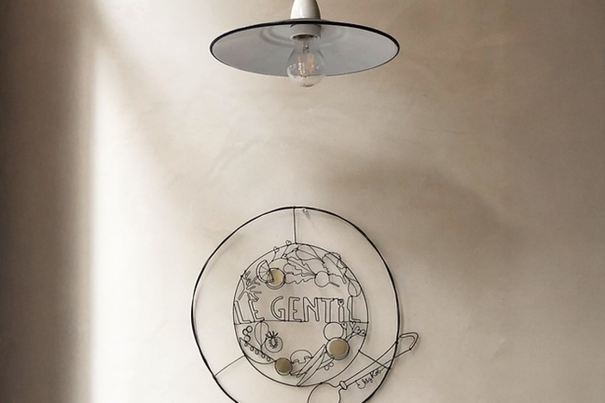 Interior wall at Le Gentil with a pendant lamp and a wire-art sign spelling 'LE GENTIL' decorated with vegetable motifs.