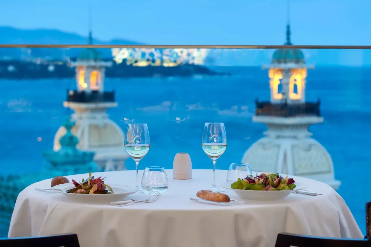 A table set for two at Le Grill on the eighth floor of Hôtel de Paris, looking over the towers of the Casino de Monte-Carlo to the sea at dusk