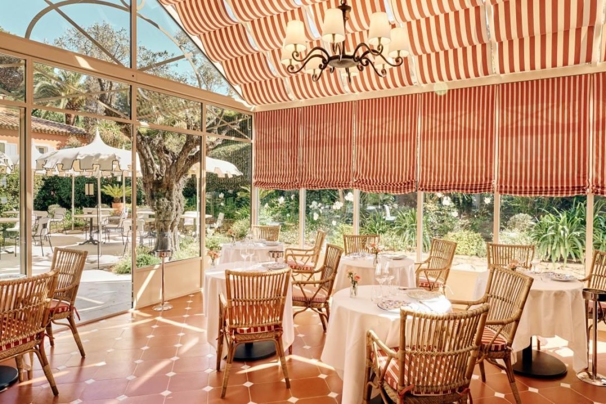 Covered terrace dining room with striped awning, wicker chairs and set tables overlooking garden
