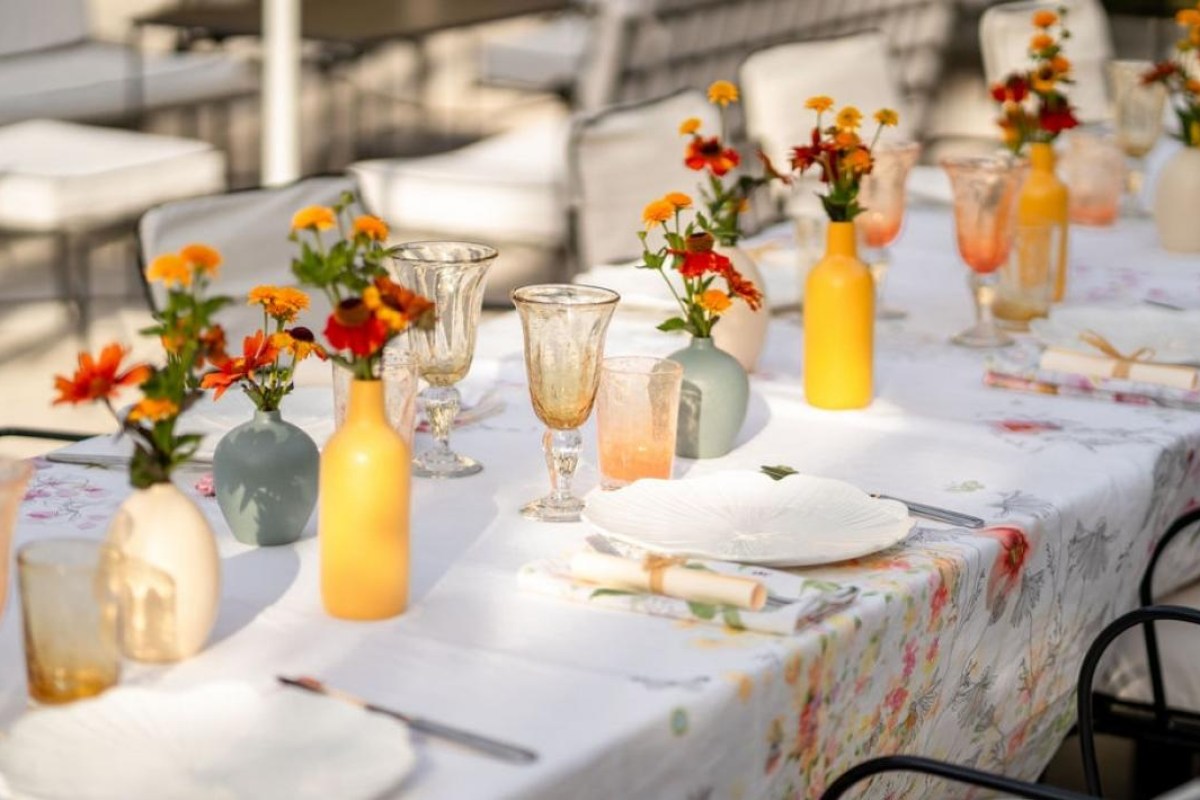 Outdoor dining table set with colorful flowers in small vases, glassware and white plates