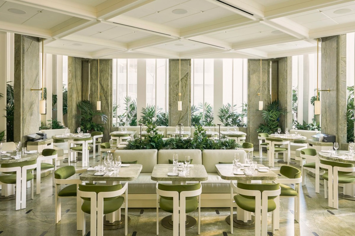 Wide view of the restaurant's dining room with marble columns, greenery, and green velvet chairs