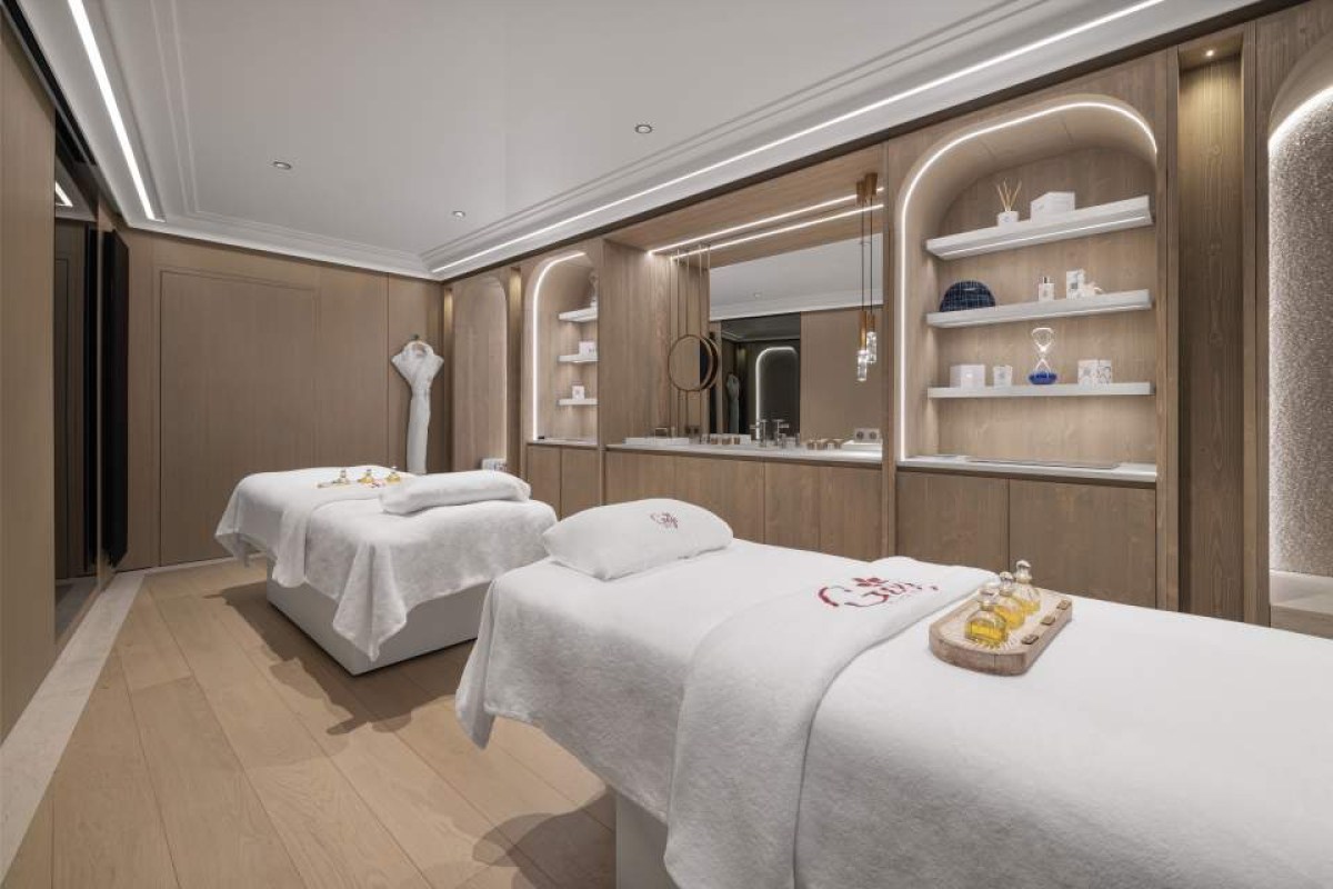 Elegant spa treatment room with two massage beds, wood paneling, and soft ambient lighting.