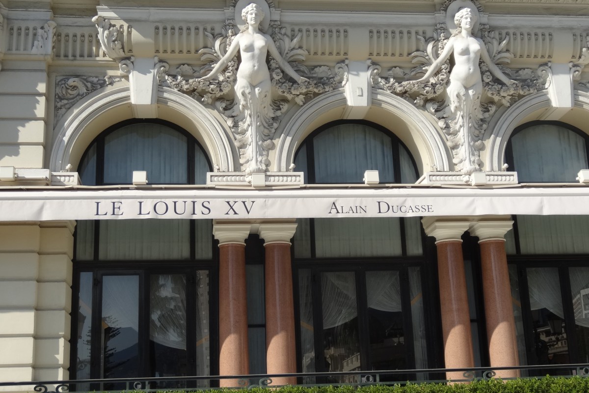 Ornate exterior facade of Le Louis XV restaurant with sculpted figures, columns, and the restaurant's name sign.