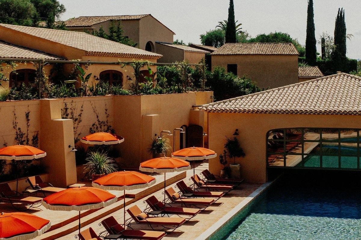 Pool terrace with orange umbrellas and loungers beside tiled-roof Provençal-style hotel buildings