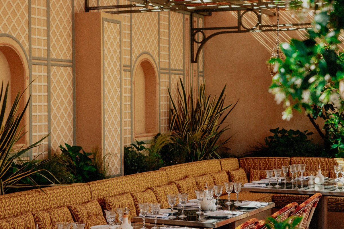 Covered outdoor restaurant terrace with patterned banquette seating and set tables against ornate trellis-patterned walls