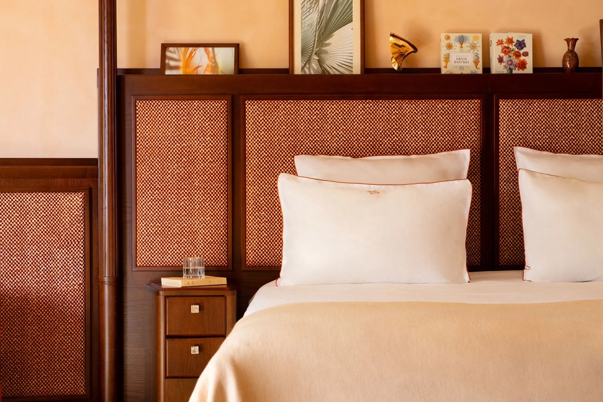 Close-up of a guest room bed with woven headboard panels, white pillows, and a wooden nightstand with decor