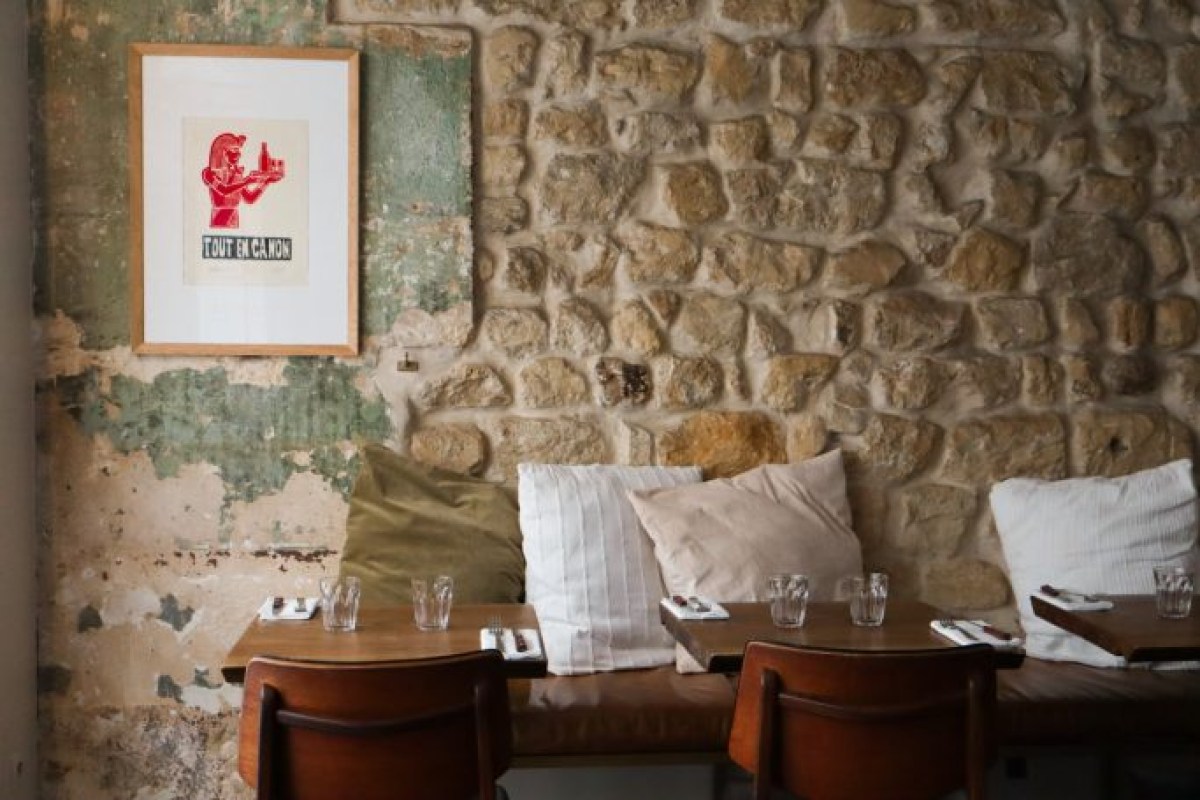 Restaurant dining room with stone wall, framed red print, cushioned bench seating and wooden tables set for dining
