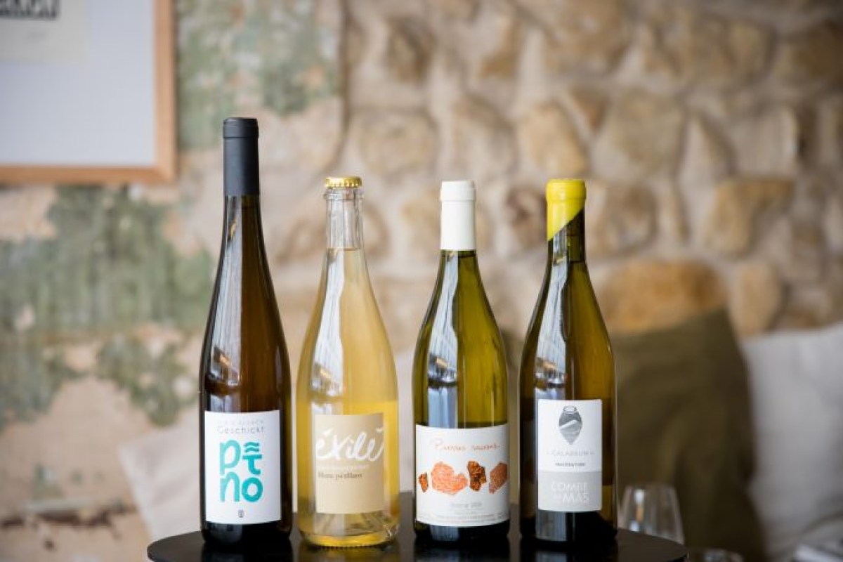 Four wine bottles lined up on a table against the restaurant's exposed stone wall backdrop