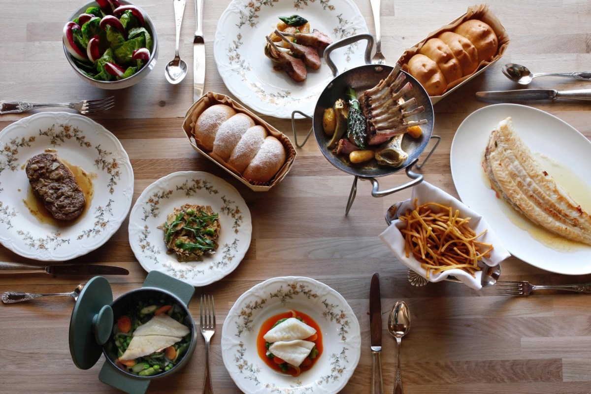 Overhead view of a laid table with lamb chops, fish fillet, steak, fries, salad and bread rolls