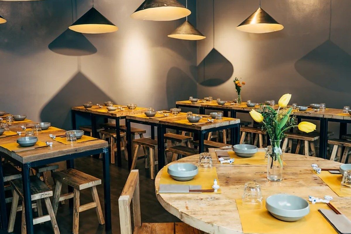 Dining room with wooden tables, gray bowls set for meals, pendant lamps, and yellow table runners