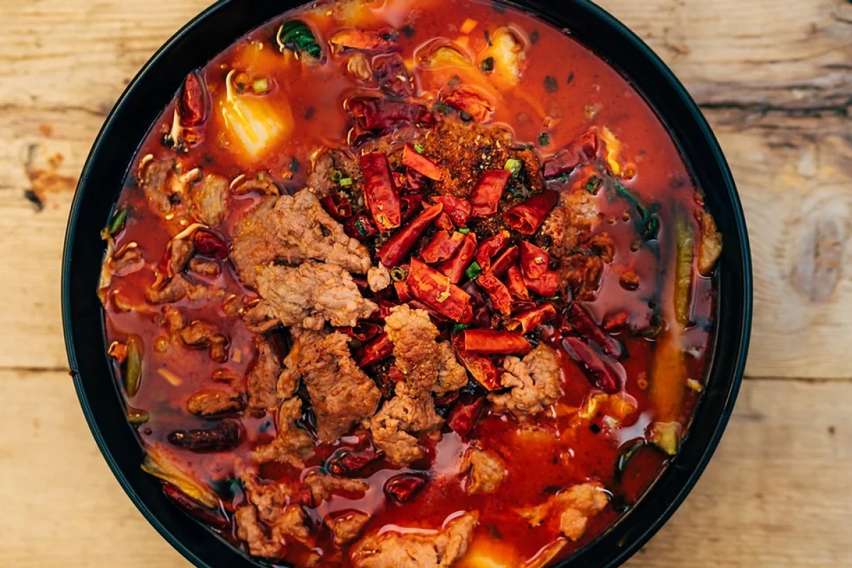 Overhead shot of a spicy red Sichuan soup bowl with beef, dried chilies, and scallions