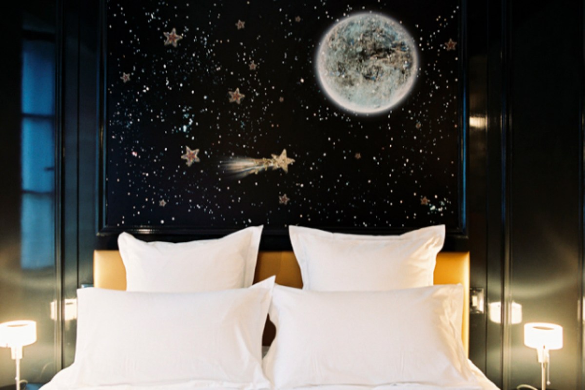 Hotel bedroom with a starry night sky mural above a white pillow-topped bed