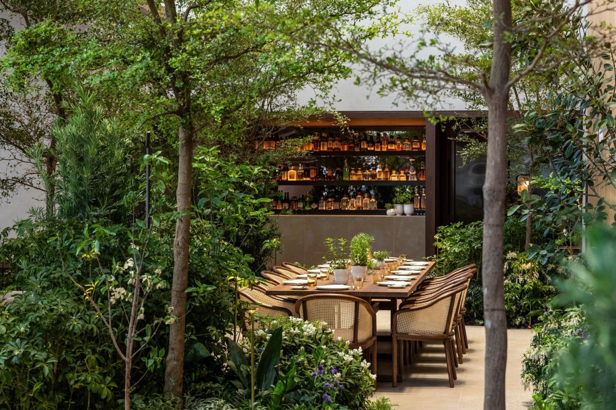 Lush garden terrace with a long dining table and glowing bar shelves surrounded by greenery