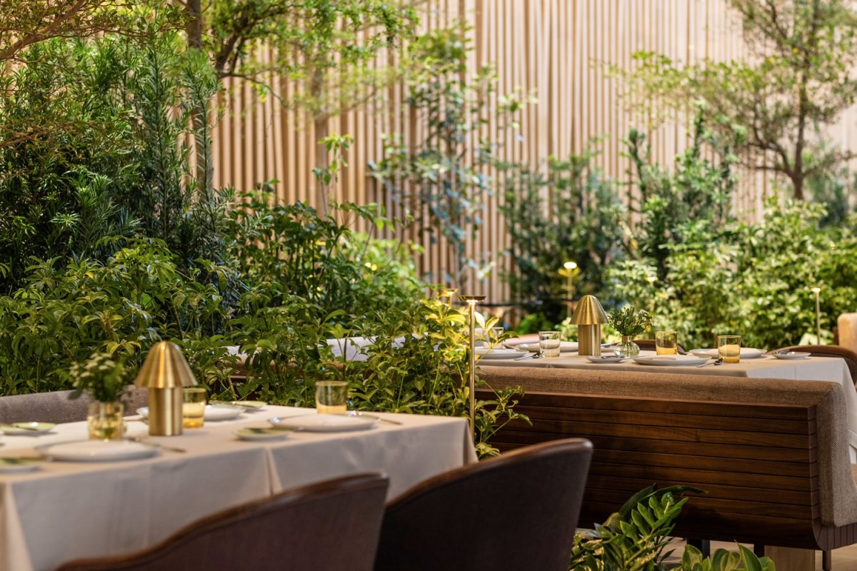 Restaurant terrace dining area with set tables among greenery and a wood slat wall