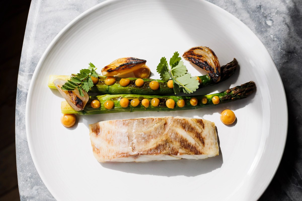Seared fish fillet with grilled asparagus, shallots, and orange sauce dots on a white plate.