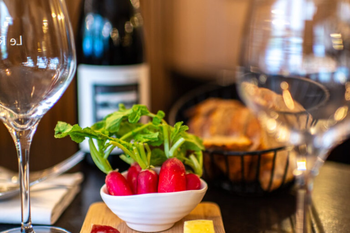 Laid table with a bowl of fresh radishes, bread basket, wine bottle and glasses