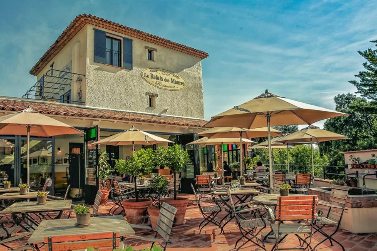 Exterior view of Le Relais des Maures with terrace, umbrellas and signage on building facade