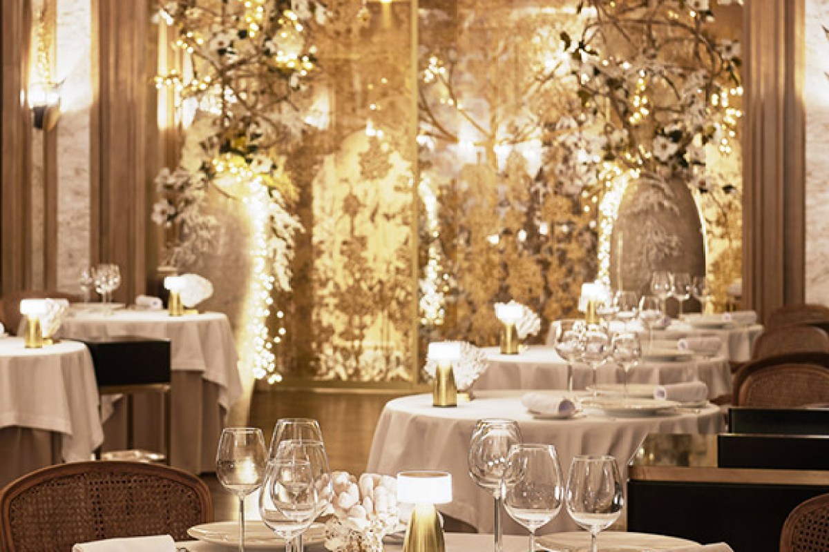 Elegant dining room with white-clothed round tables set with glasses, candles and floral lighted backdrop