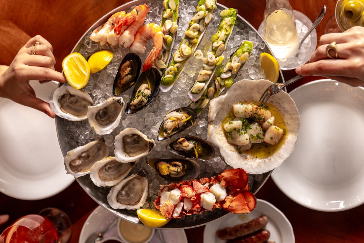 Overhead view of seafood tower with oysters, shrimp, mussels, lobster and scallops, hands reaching in