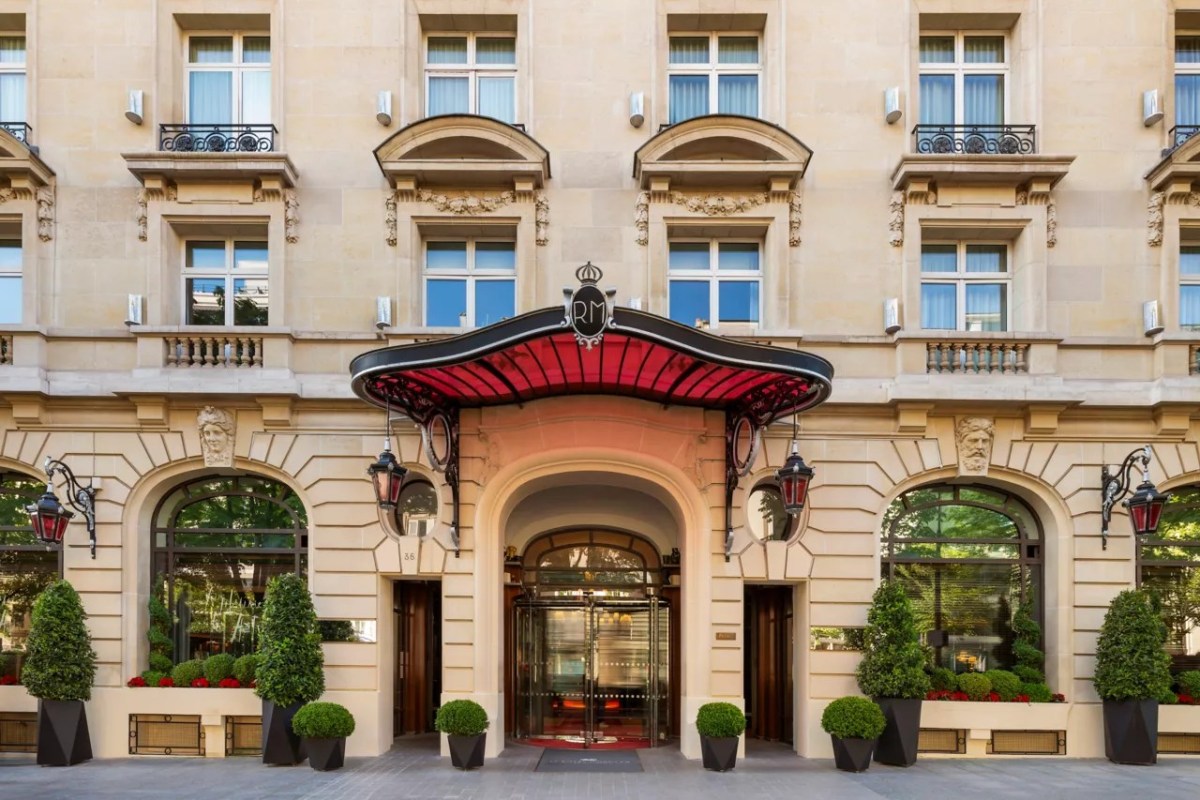 Hotel's ornate limestone facade with red glass canopy over revolving door entrance, Paris street