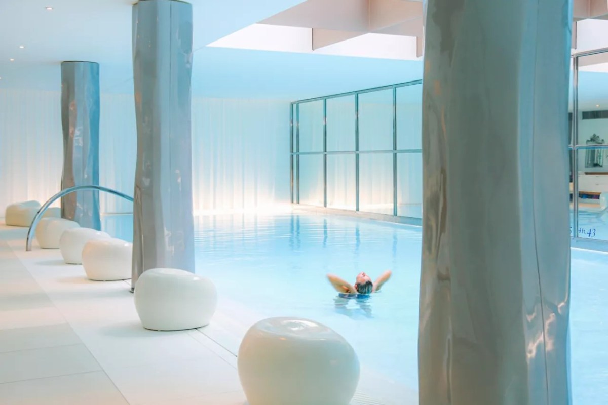 Indoor spa pool with sleek columns and a person floating in calm blue water