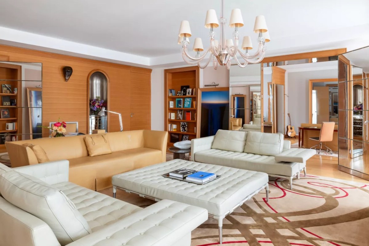 Spacious hotel suite living room with cream leather sofas, a chandelier, and mirrored wood paneling