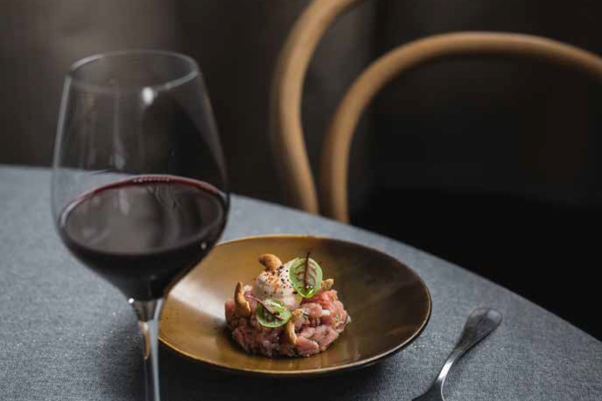 Table setting with a glass of red wine beside a tartare dish on a dark plate