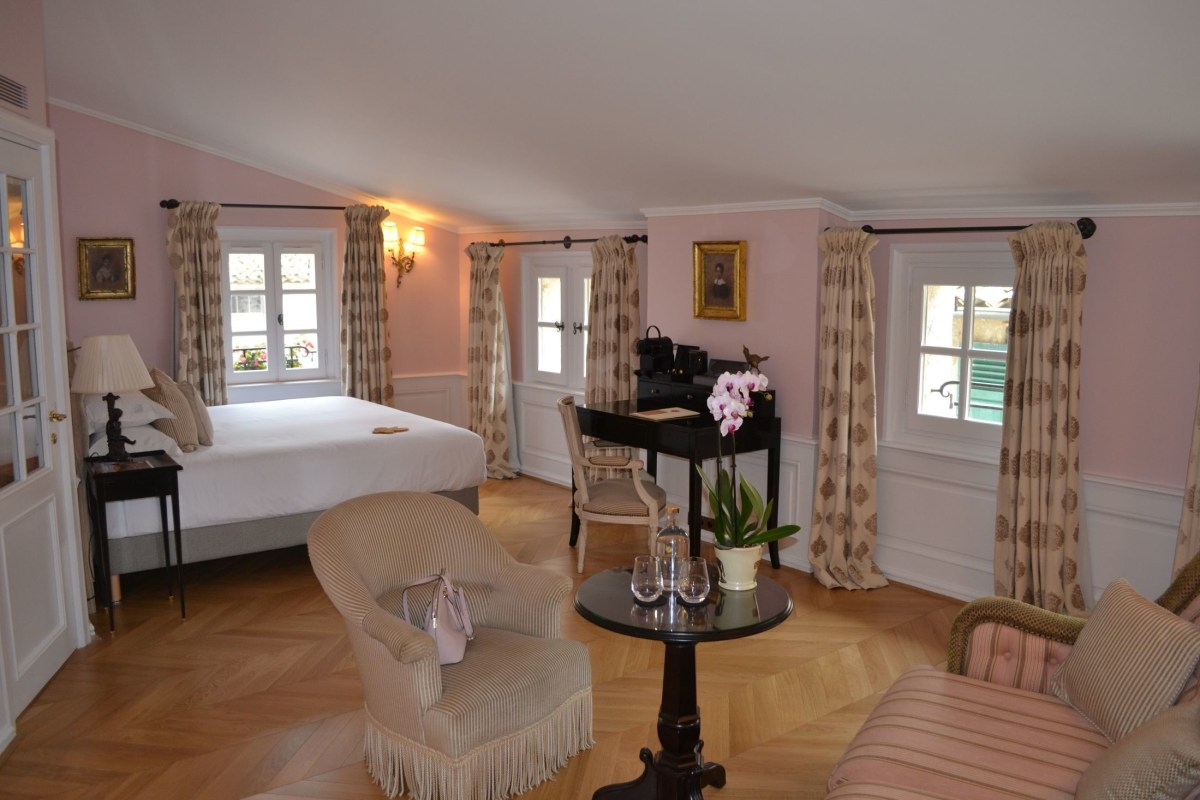 Spacious pink-toned suite with four-poster style bed, desk and French windows