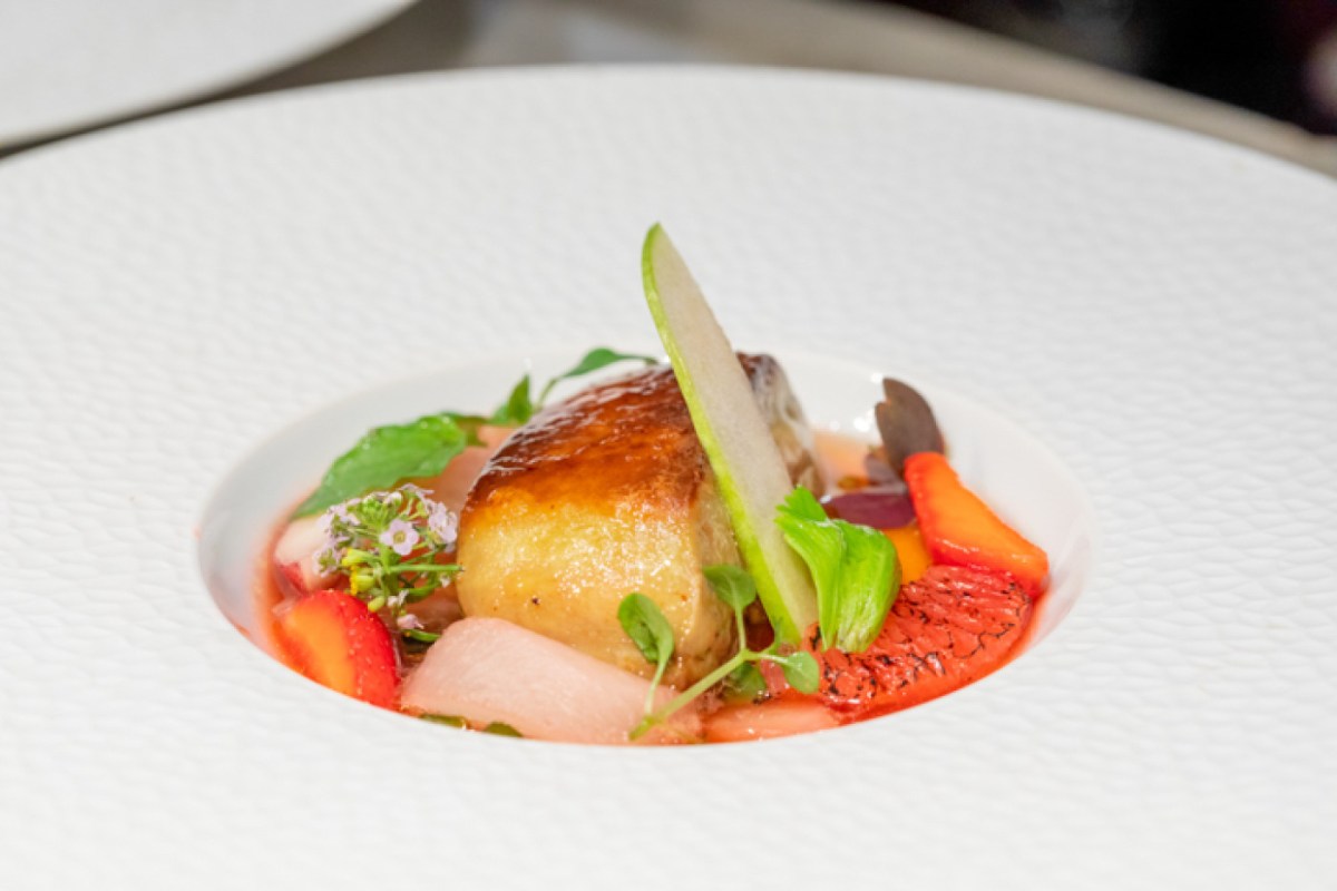 Elegant plated dish with foie gras, apple slice, strawberries and herbs on white plate