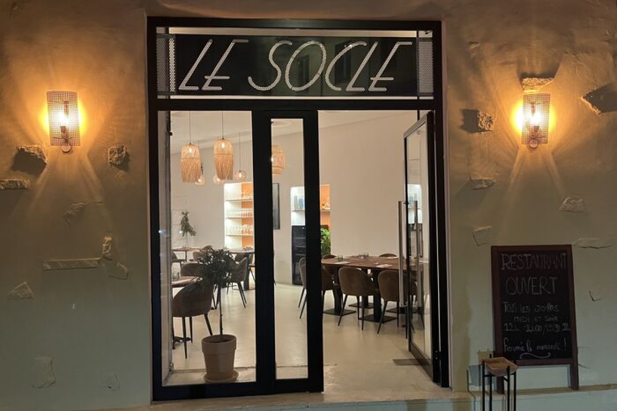 Entrance of Le Socle restaurant at night, glass door with illuminated sign and view into dining room