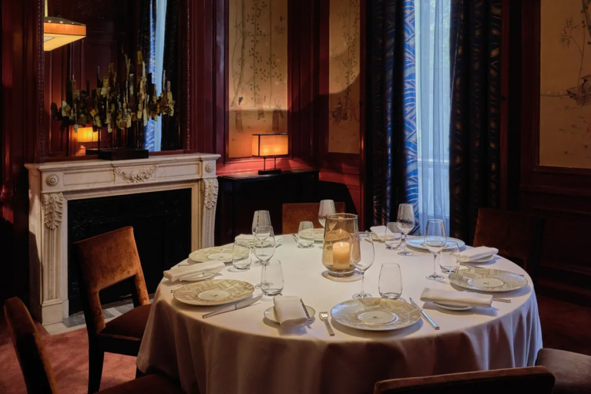 Elegant dining room table set with white linens, glassware, and candlelight near a marble fireplace
