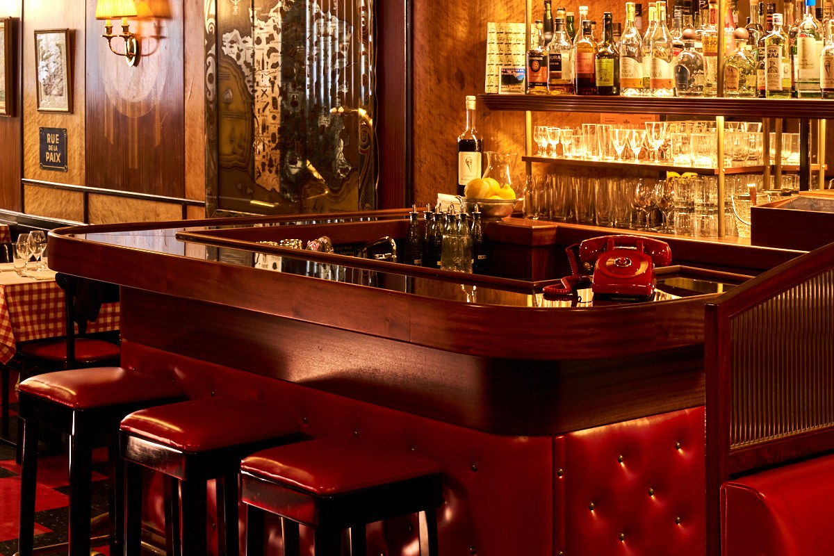 Le Veau d'Or bar counter with red leather stools, red rotary phone, bottles and glassware on shelves