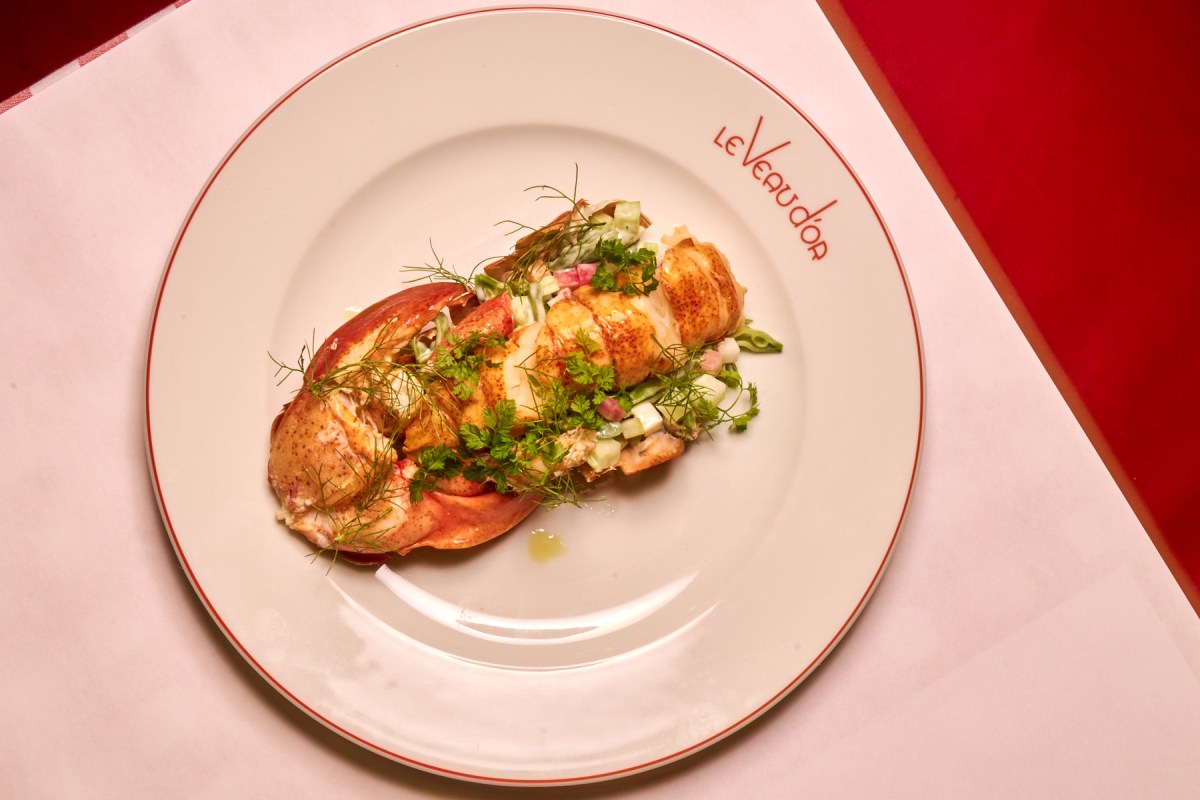 Lobster dish with herbs on a white plate with red rim reading 'Le Veau d'Or'