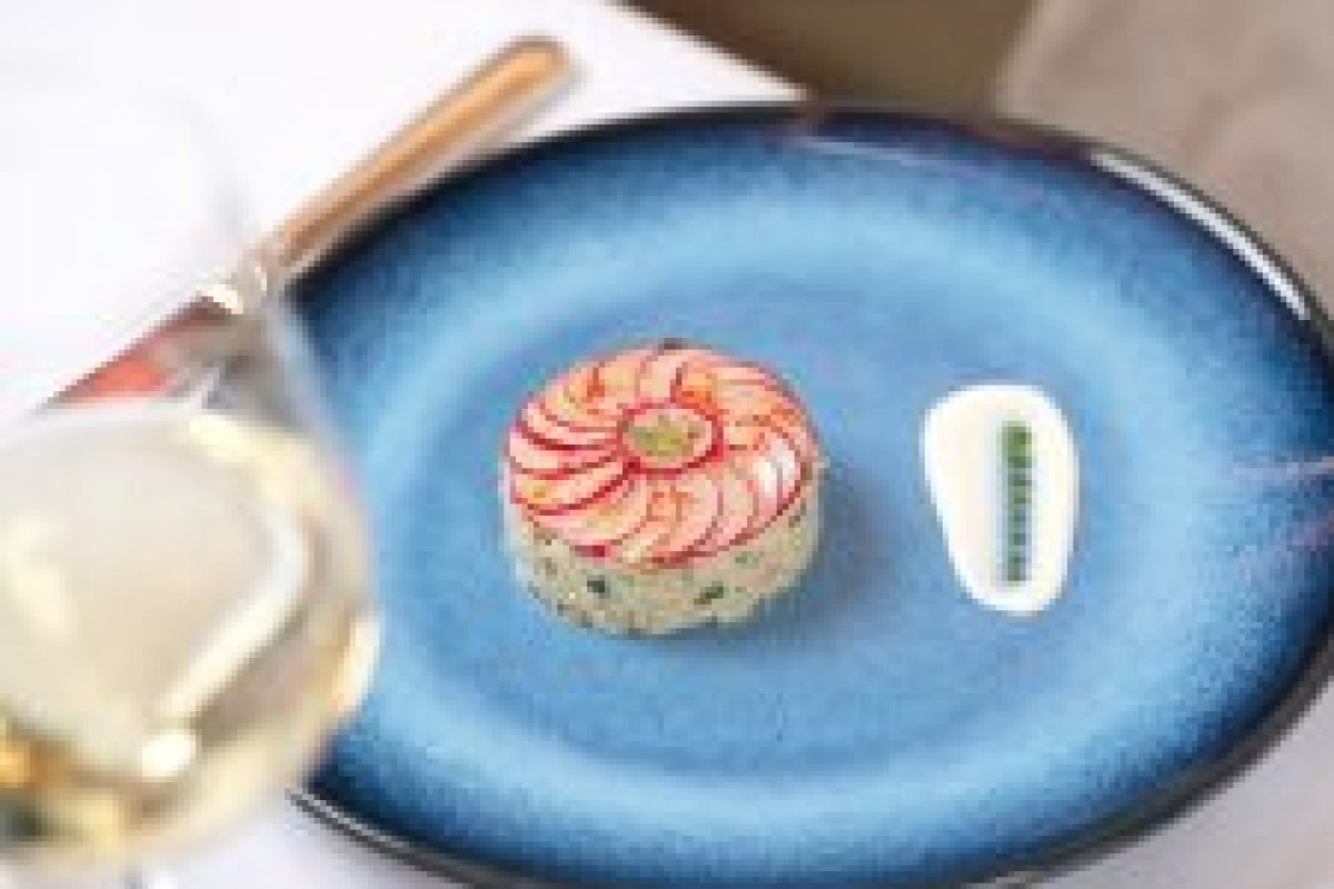 Delicate tartare dish artfully plated on a blue oval plate with a wine glass in frame.