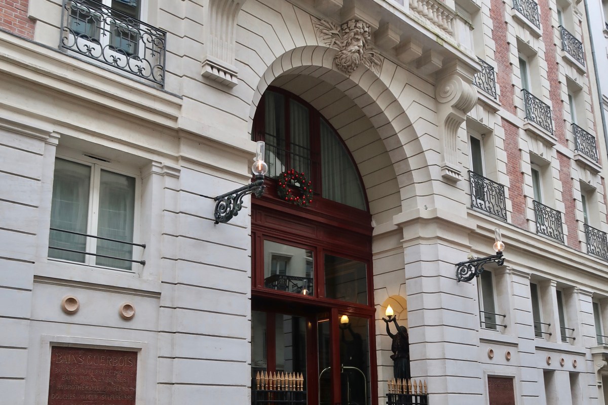 Full view of Les Bains Paris entrance arch with carved mask, iron balconies, wreath and lantern.