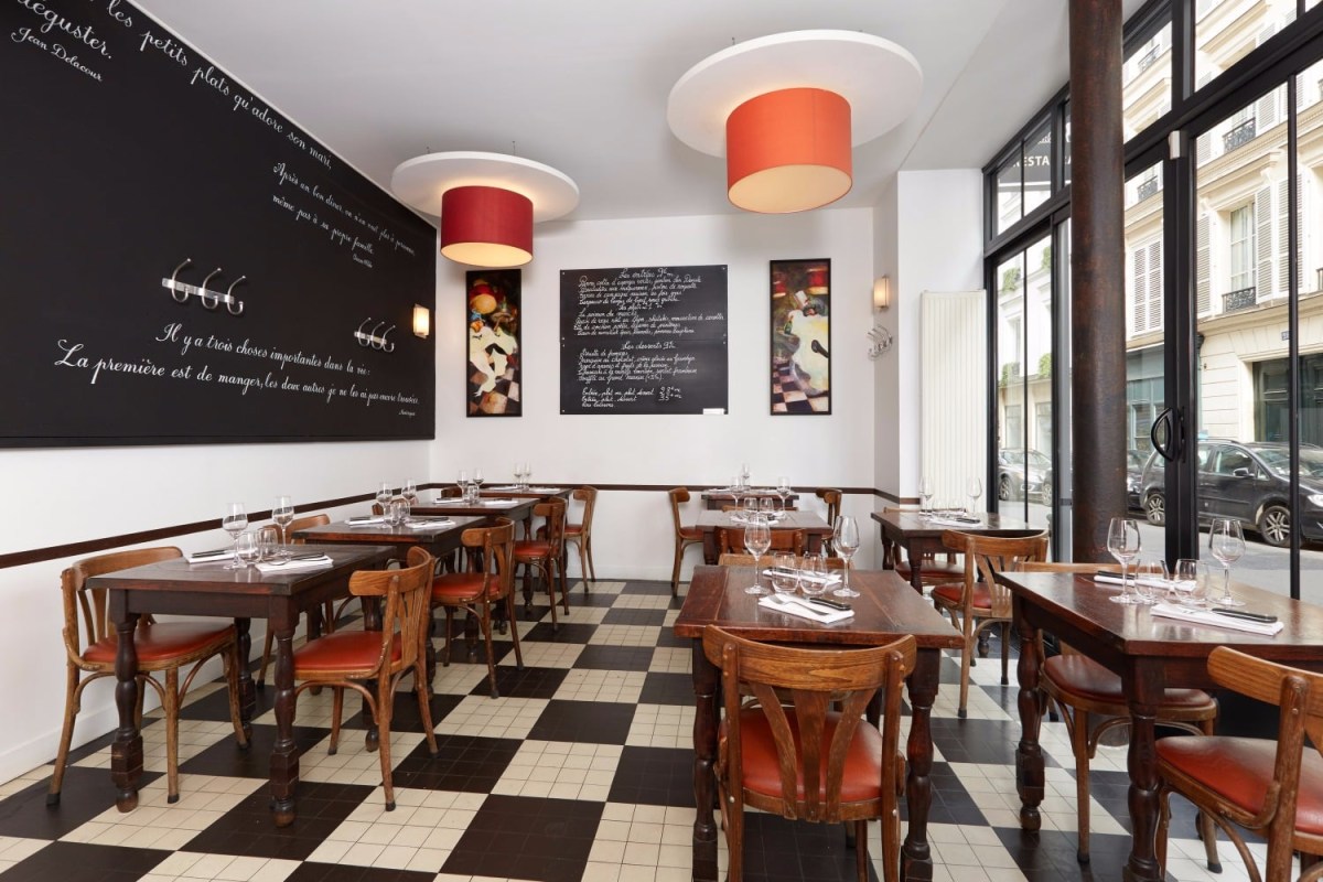 Dining room with black-and-white checkered floor, wooden tables, orange chairs and chalkboard wall