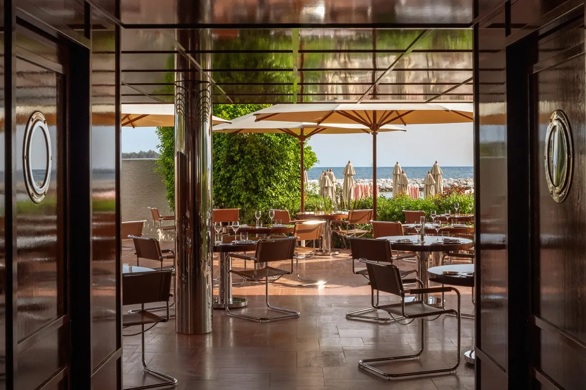 The dining room of Les Pêcheurs at the Cap d'Antibes Beach Hotel, with chrome columns and leather chairs opening onto a terrace by the sea