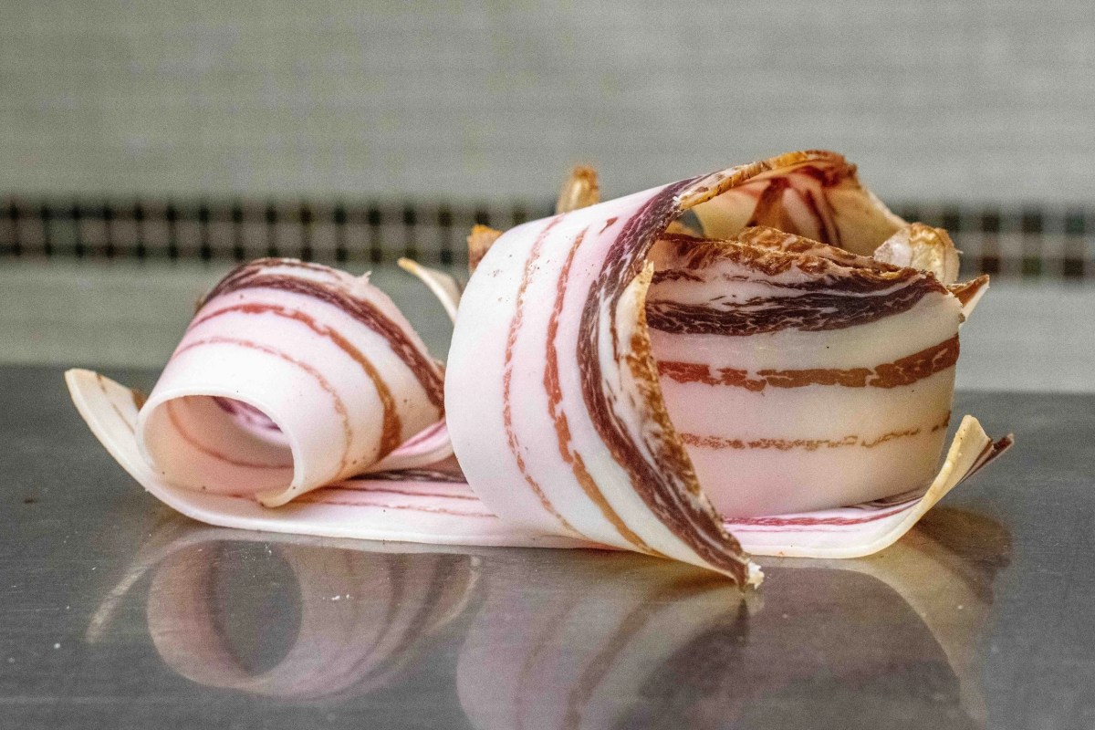 Thinly sliced cured ham rolled into decorative shapes on a metal surface