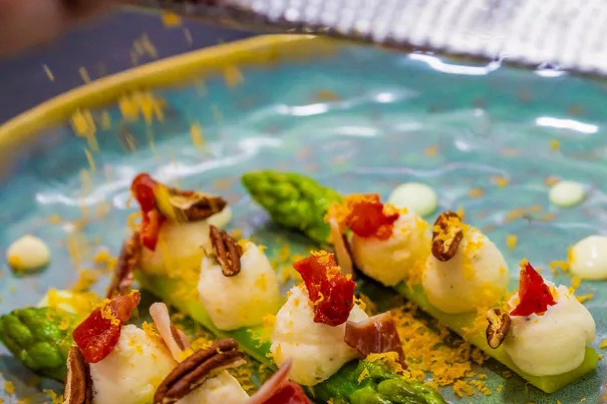 Close-up plated dish of asparagus spears with goat cheese, cured ham, pecans and candied pepper on a teal plate