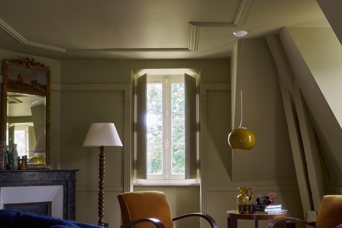 Elegant suite corner with armchairs, lamp, and shuttered window overlooking trees