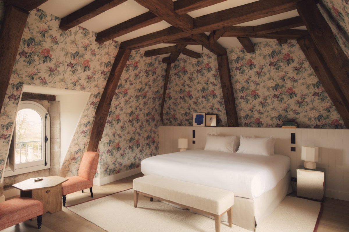 Guest room with exposed wood beams, floral wallpaper, white bed, and pink accent chairs