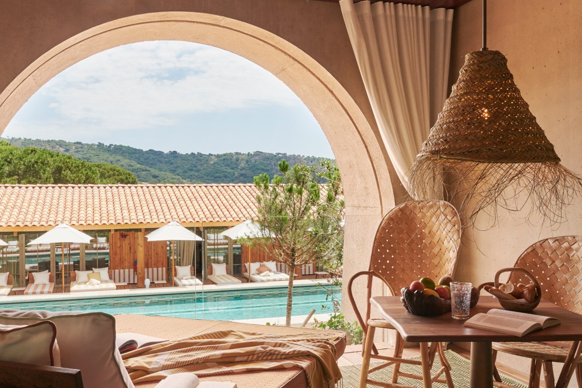 Terrace dining table framed by stone arch overlooking pool and loungers
