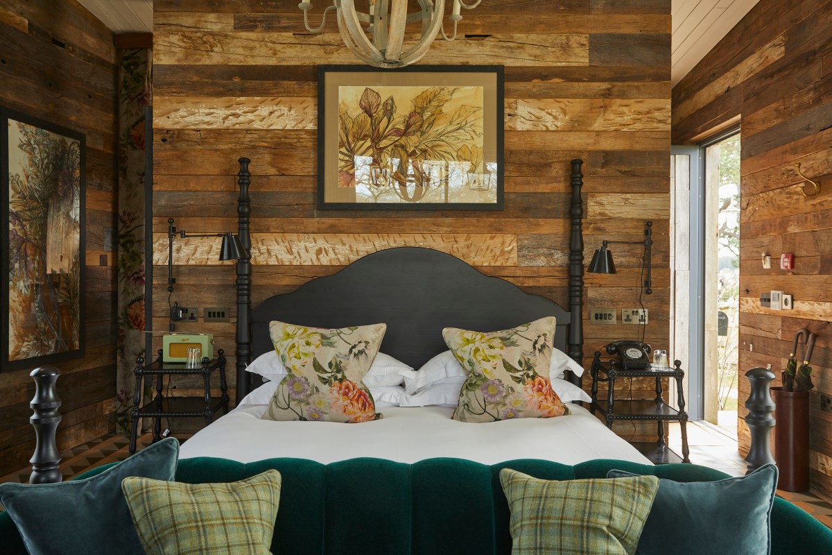 Rustic guest room with reclaimed wood walls, four-poster bed, and floral cushions